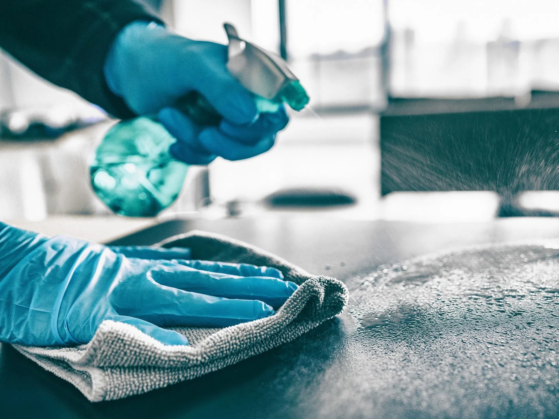 A cleaner in gloves spraying and wiping down a countertop