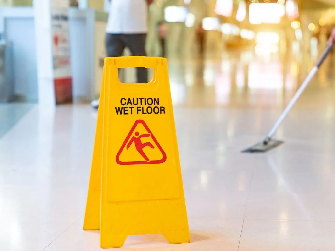 A wet floor sign beside a mop in a commercial corridor