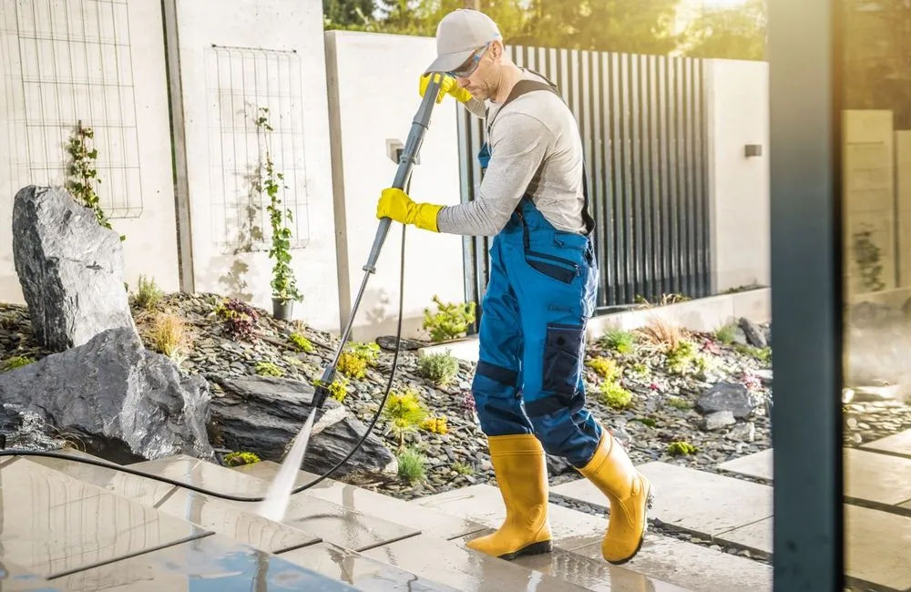 A worker pressure washing a paved patio