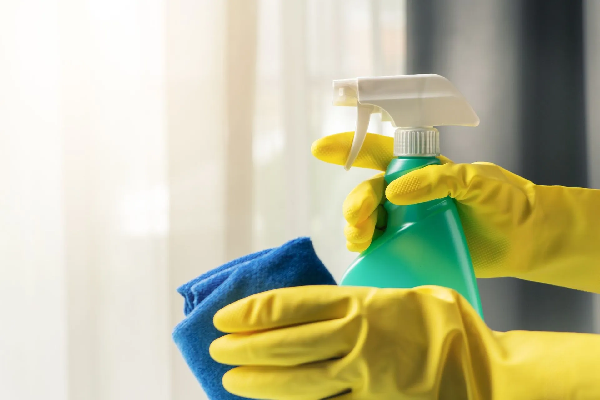 Gloved hands holding a spray bottle and a microfibre cloth