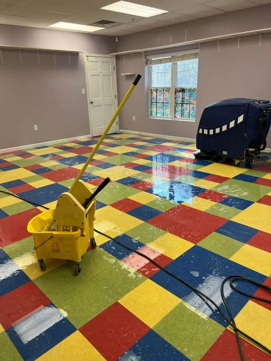 A classroom floor mid-scrub, with a mop bucket and a ride-on scrubber